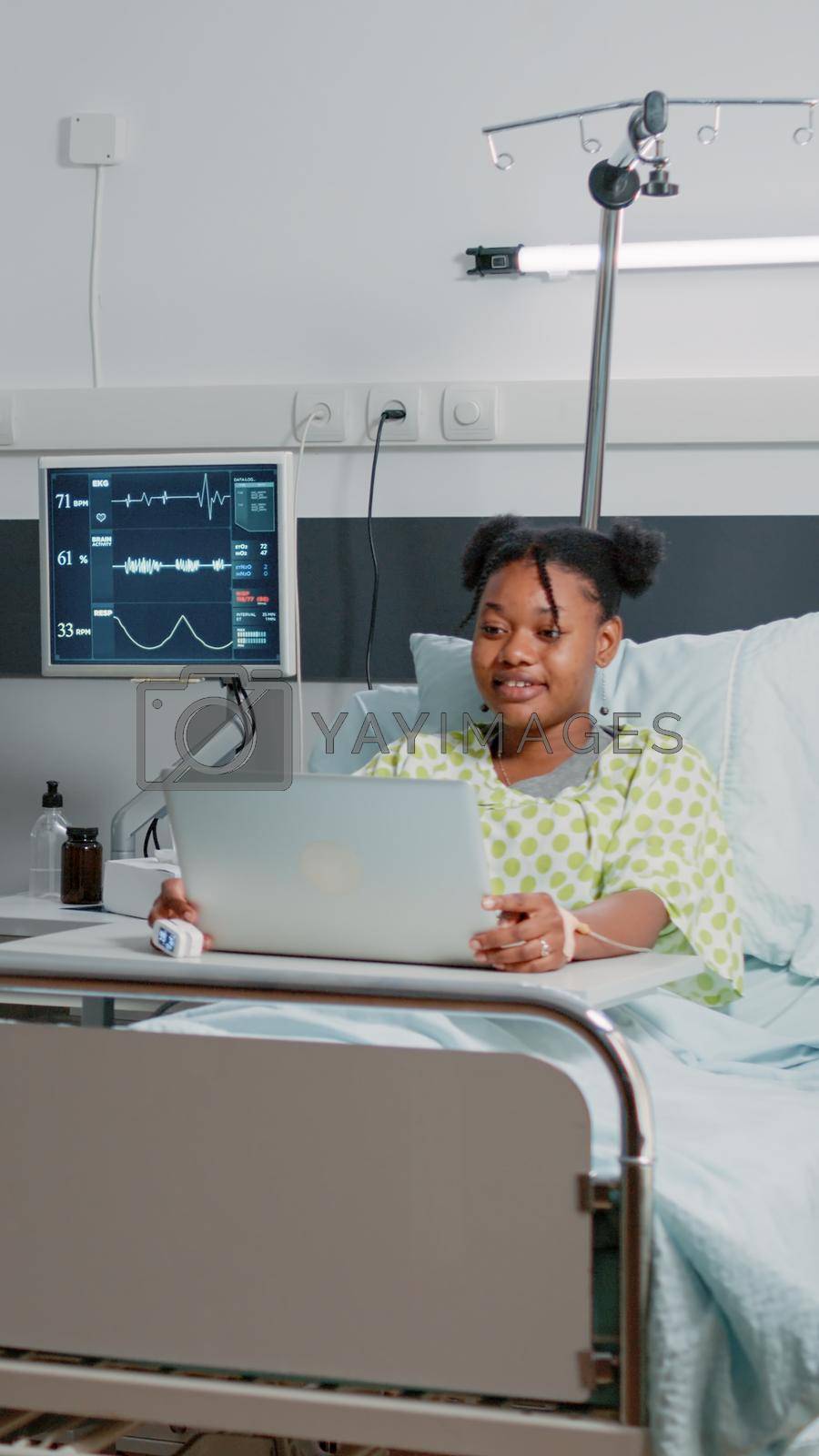 Young patient using video call on laptop for remote communication while sitting in hospital ward bed. Woman talking to friends on online video conference conference about healthcare.