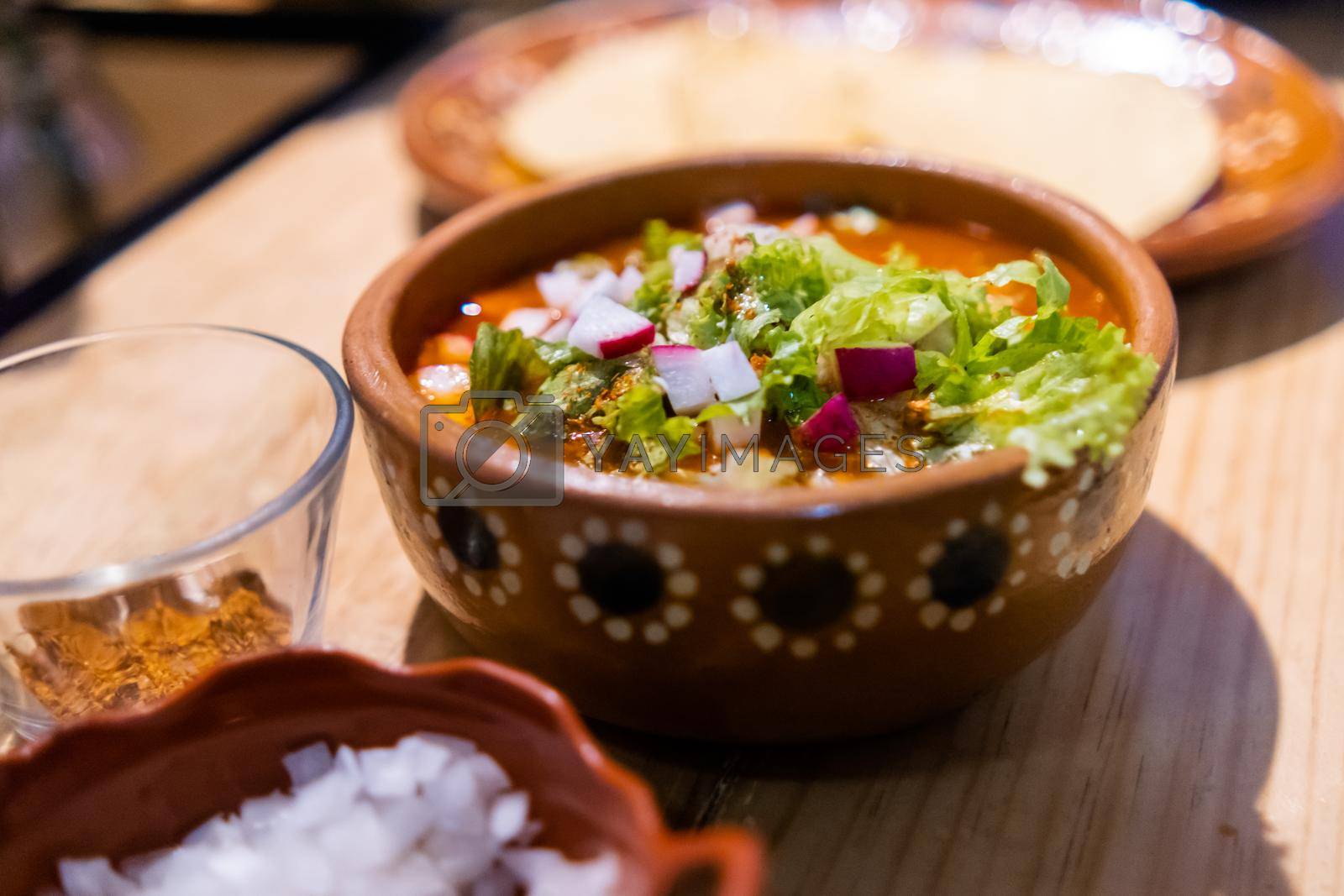 Royalty free image of Clay bowl of delicious and traditional Mexican pozole on wooden table by Kanelbulle