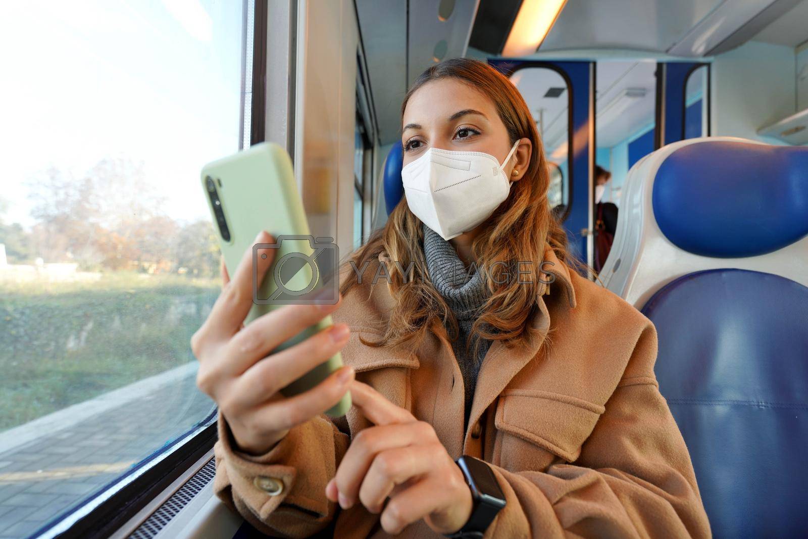 Omicron Variant. Woman traveling on train wearing medical protective face mask using smartphone. Low angle.