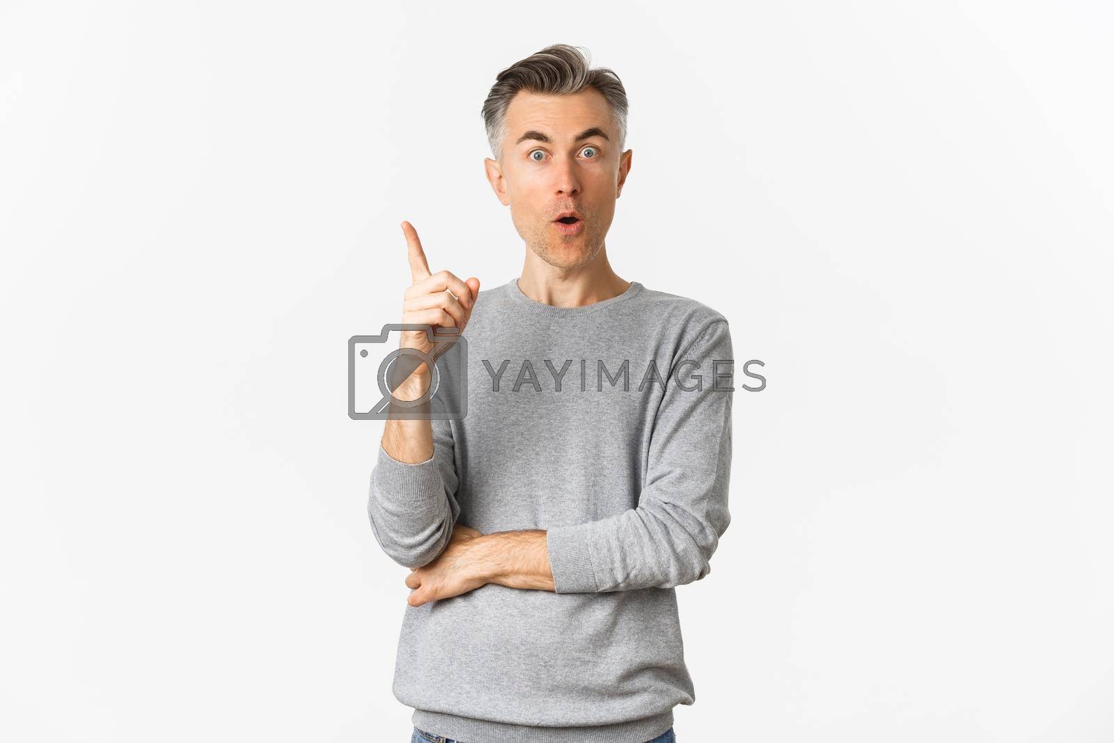 Royalty free image of Portrait of thoughtful adult male model with short grey hair, raising finger up, having an idea, say suggestion, standing over white background by Benzoix