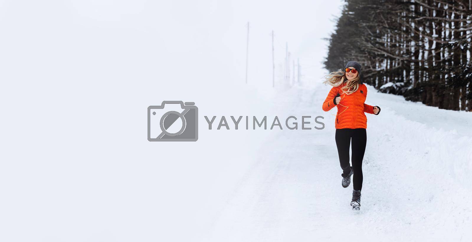 Young Sportive Woman Running Along the Way Near the Forest. Workout Outdoors in Winter. Photo with Copy Space. Sport Life Concept.