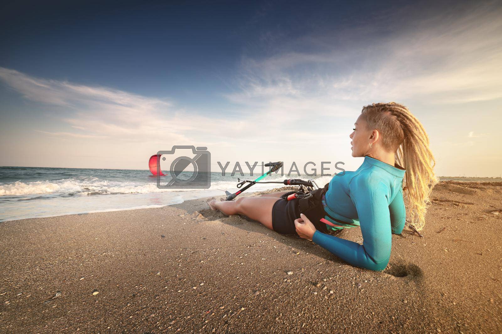 Royalty free image of Attractive caucasian woman with dreadlocks on her head in a wetsuit lies on a sandy beach and holds her kite. Water sports. Kite surfer on vacation. Copy space by yanik88