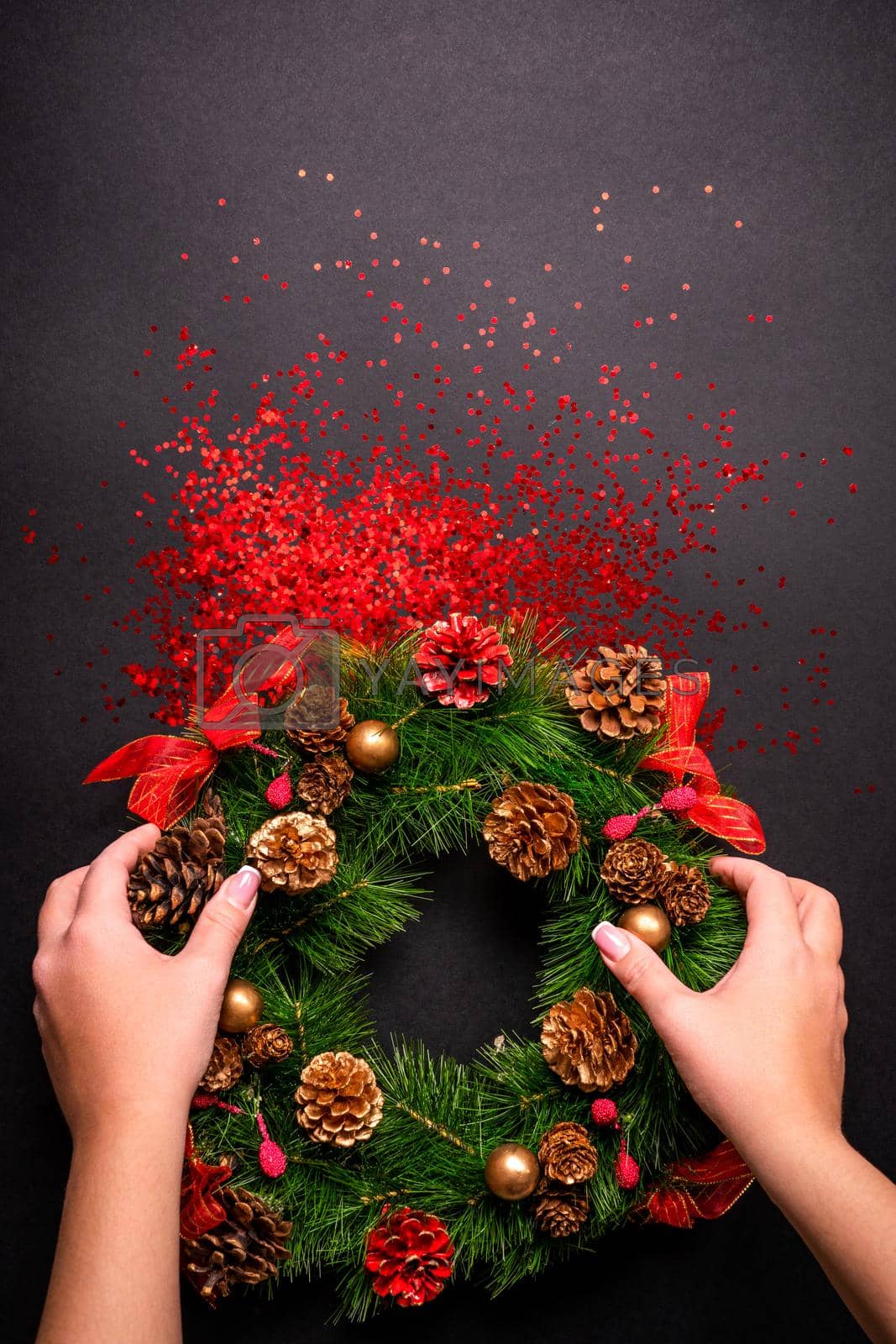 Royalty free image of Female hands holding christmas wreath over black background with glitter and copy space by Mariakray