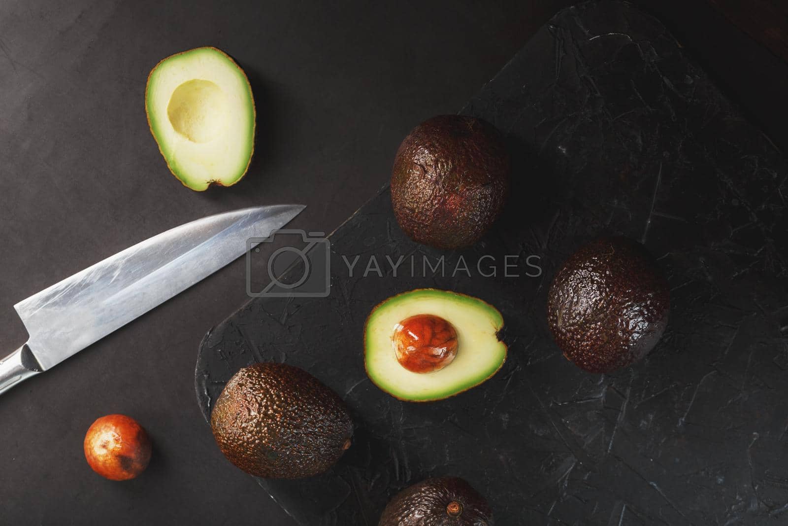Royalty free image of Sliced and whole organic avocado Hass with a knife on a black background. by AlexGrec