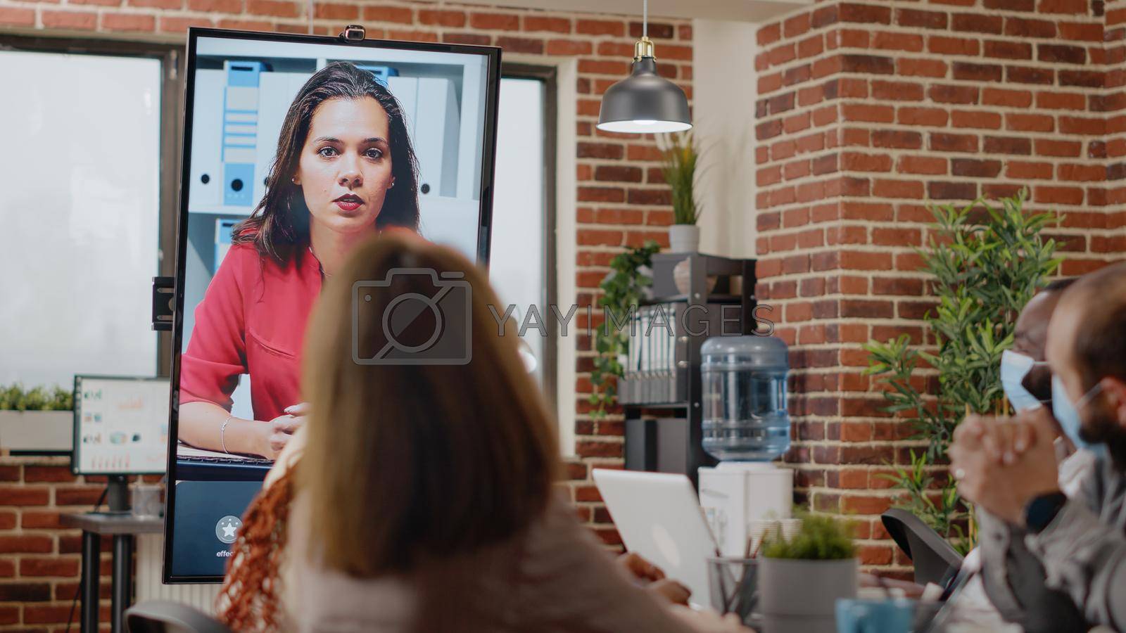 Close up of workmates using video call online communication with woman in office, talking on remote video conference chat. Multi ethnic colleagues working with teleconference meeting.