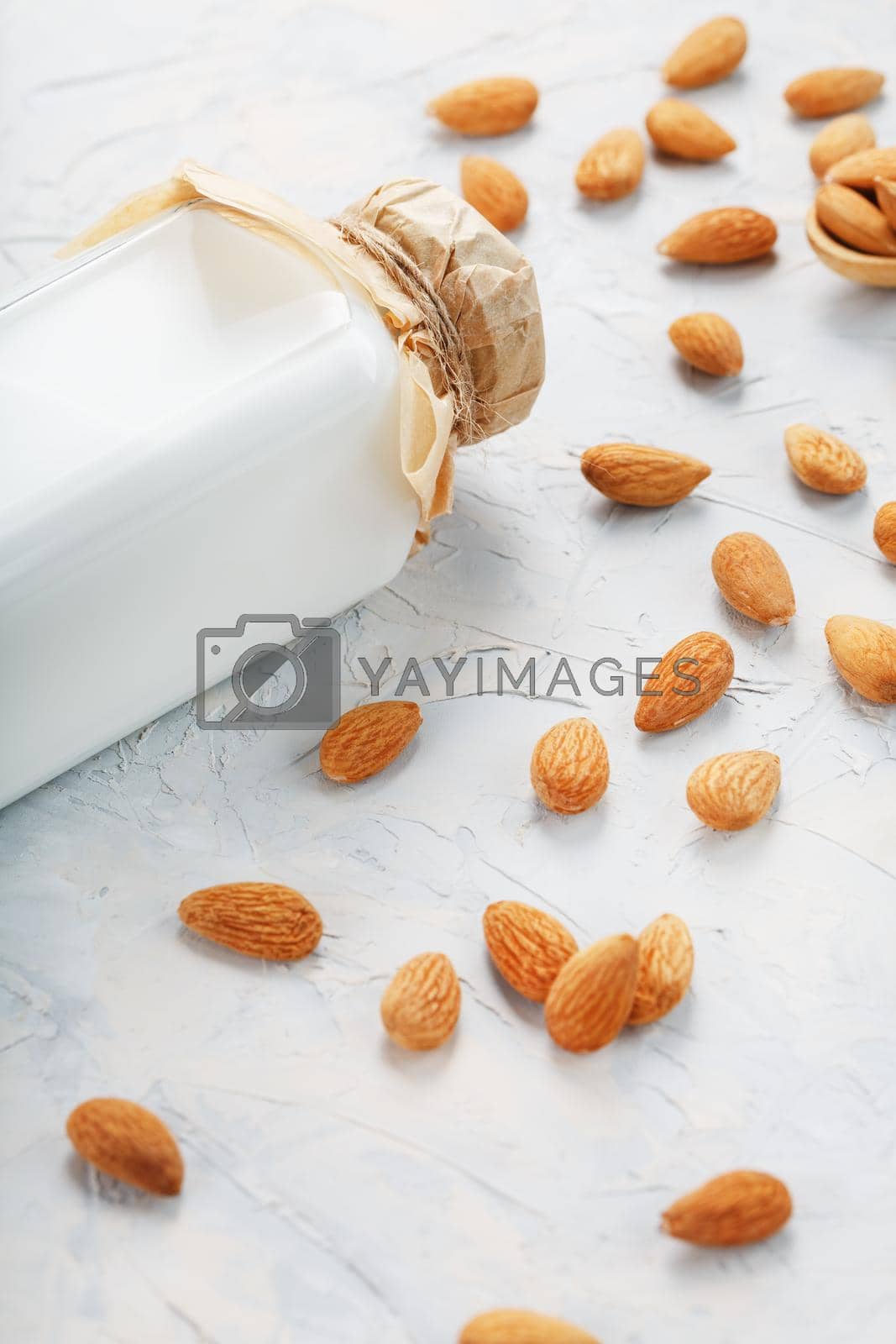 Royalty free image of Almond milk in a glass bottle on a light background with a scattering of seed kernels and a wooden spoon. by AlexGrec