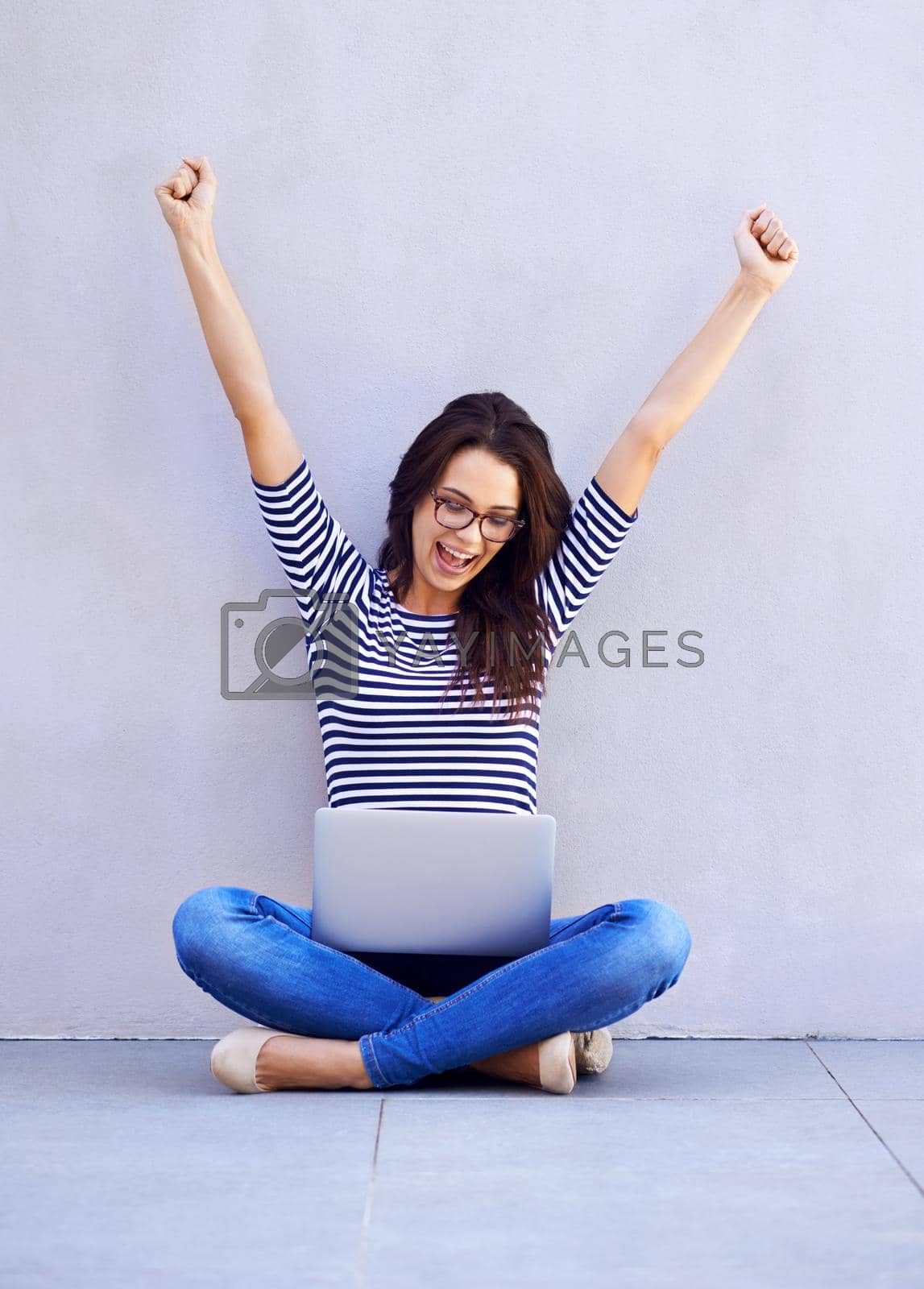 Royalty free image of Voted the number one blogger. A young woman raising her arms in celebration while looking down at the screen of her laptop. by YuriArcurs