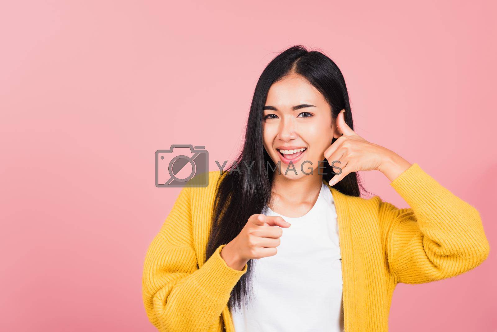 Royalty free image of woman smiling doing phone gesture with hand fingers on telephone and pointing by Sorapop