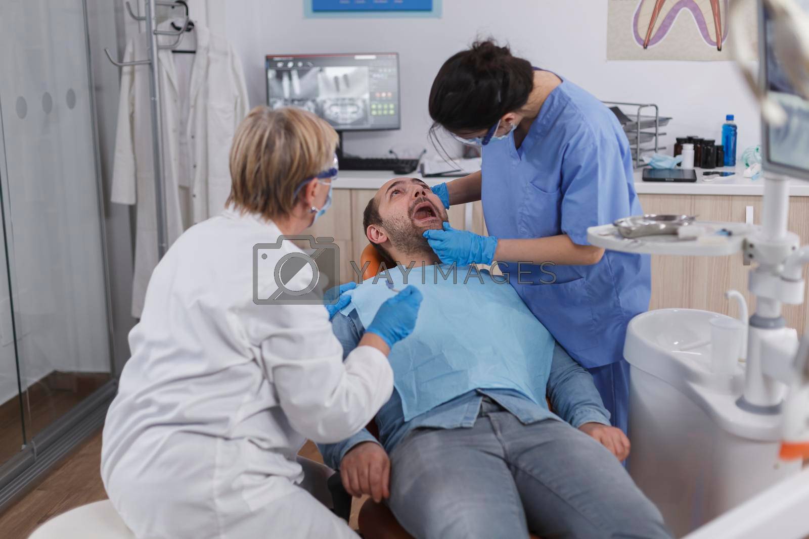 Dentist woman nurse checking patient mouth analyzing teeth infection using stomatological drill instrument during orthodontic examination in dental office room. Concept of dentistry procedure