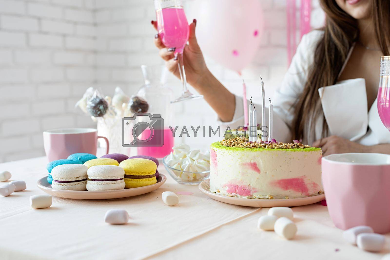 Birthday party. Birthday tables. Attractive woman in white party clothes preparing birthday table with cakes, cakepops, macarons and other sweets, having drink