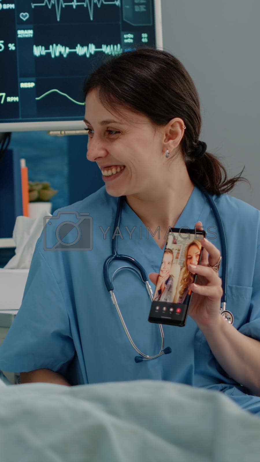 Senior woman talking to family on video call communication in nursing home. Nurse holding smartphone with online remote conference for patient in bed with disease, giving assistance.