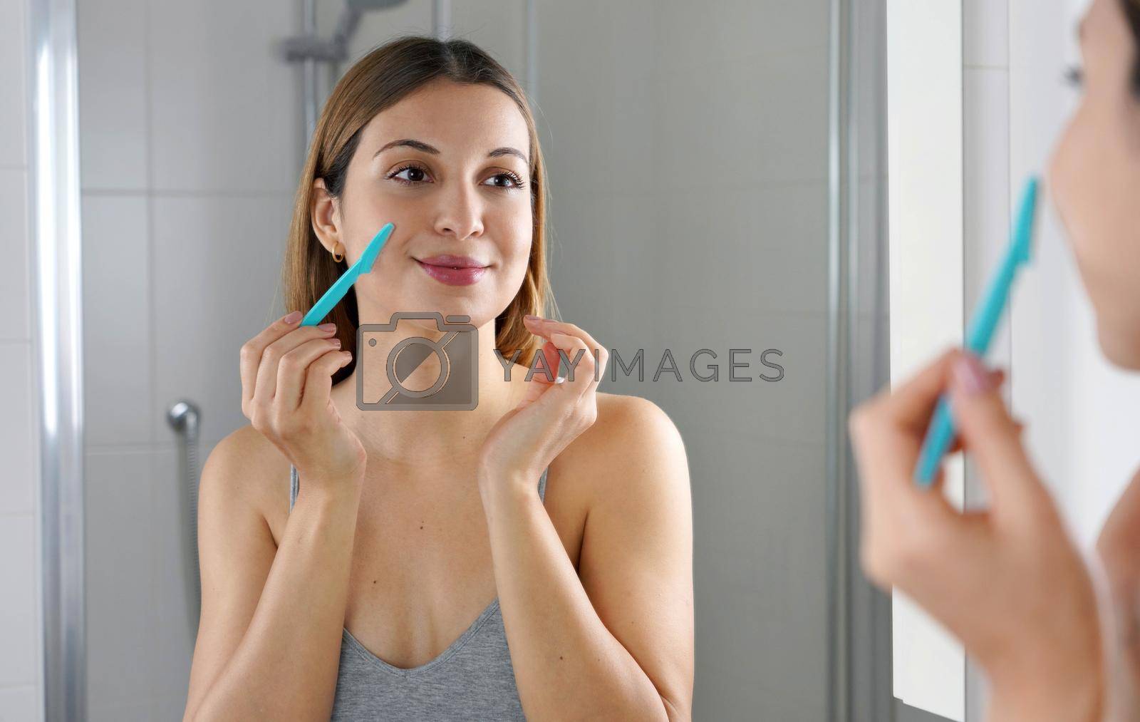Beauty woman shaving her face by razor at home. Pretty girl using razor on bathroom. Facial hair removal.