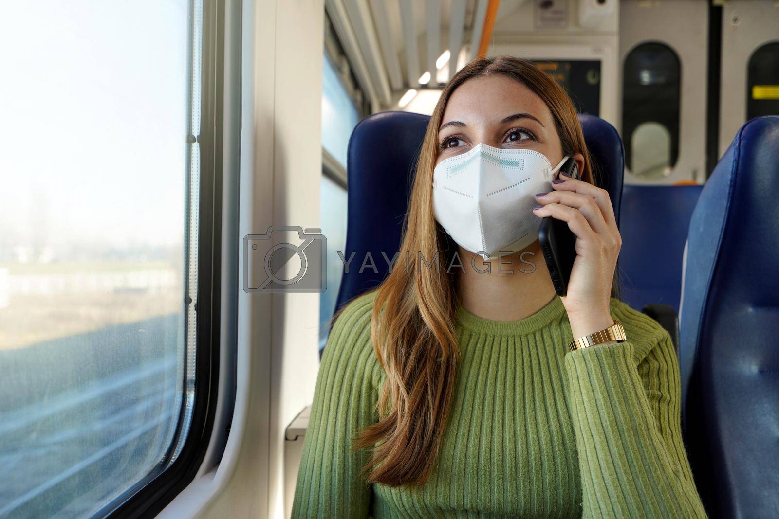 Young business woman wearing protective mask required for public transport talking with phone sitting in the train