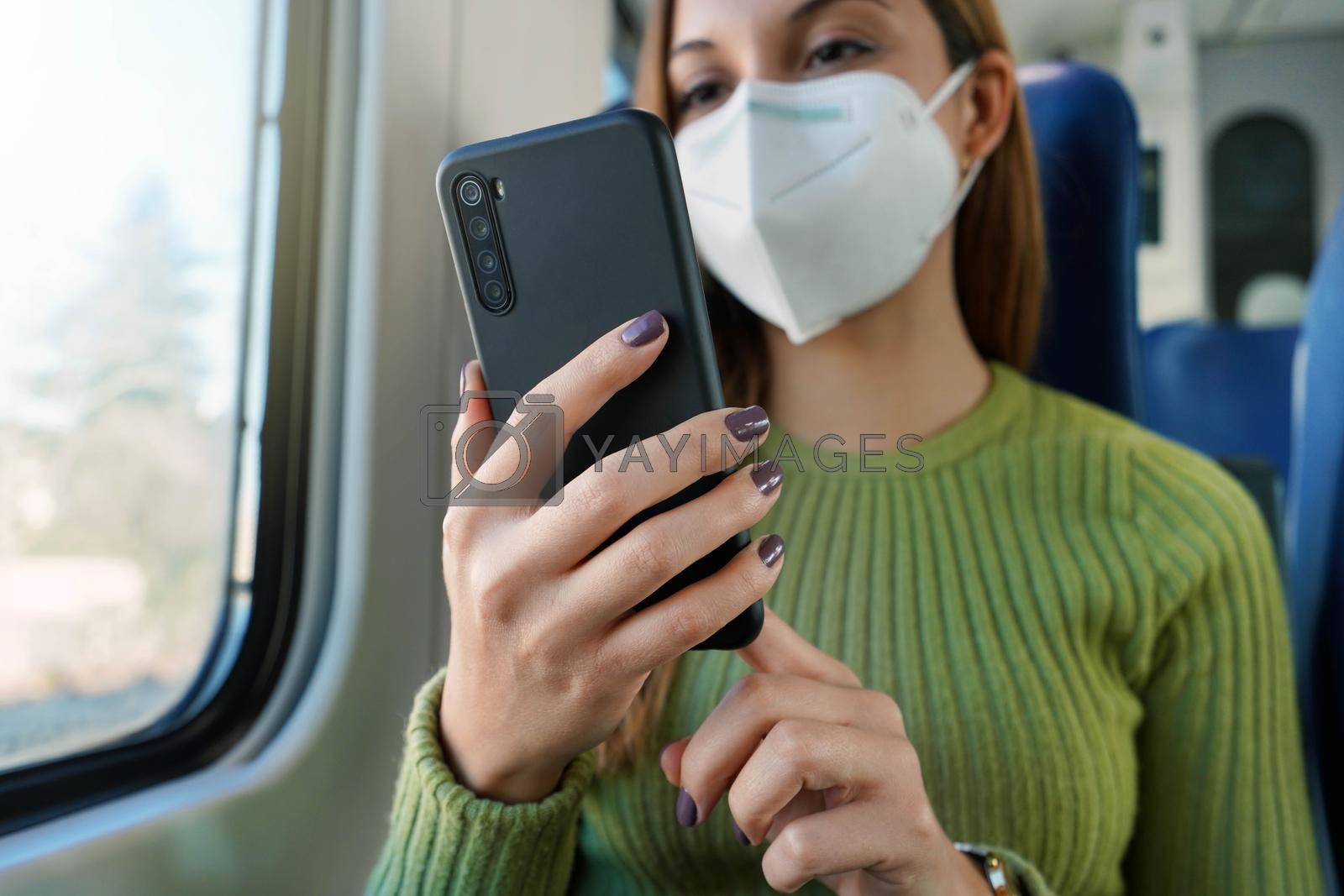 Train passenger using smartphone app during travel commute wearing protective face mask. Focus on the phone.