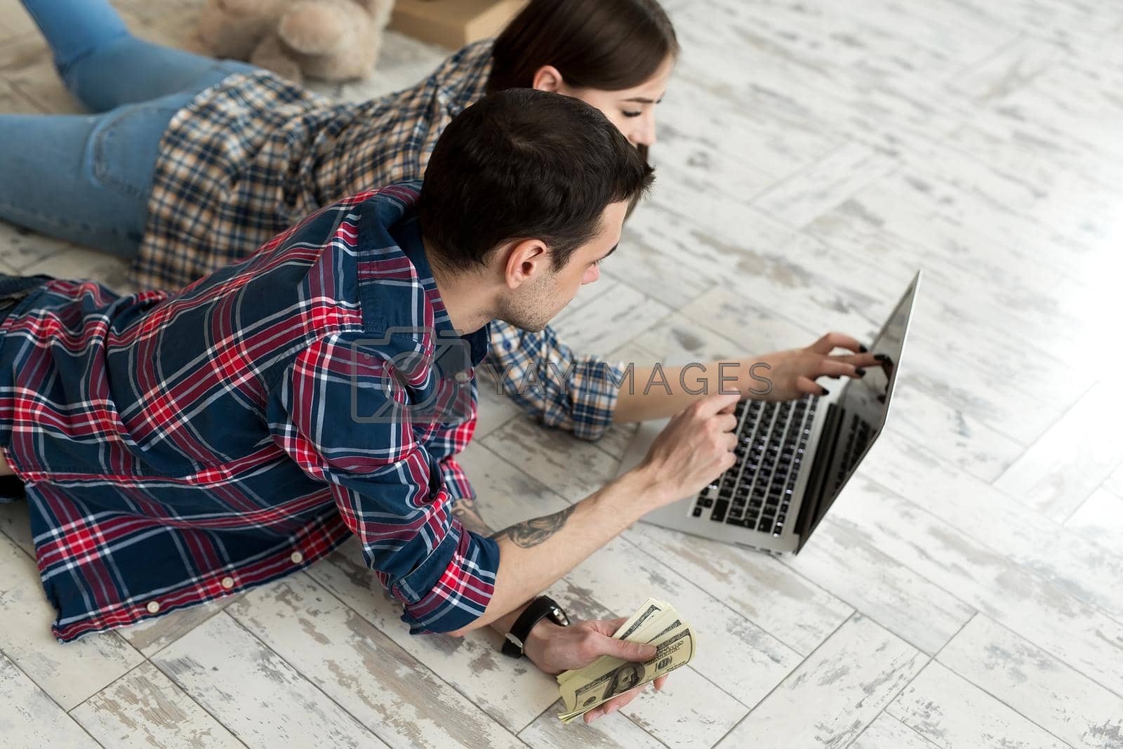 Royalty free image of Portrait of a cute young couple lying on the floor at home and managing budget using laptop. by StudioPeace