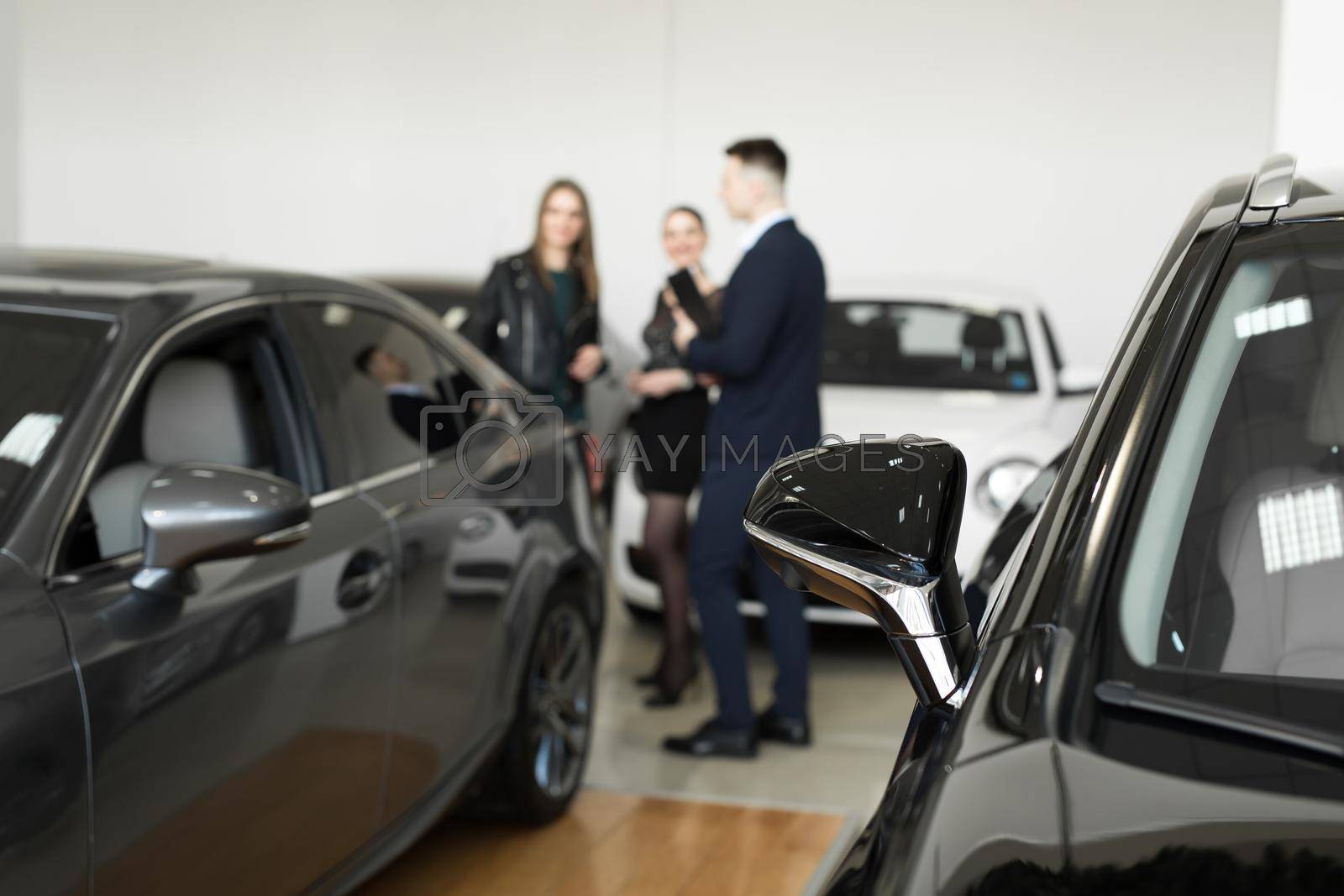 Royalty free image of Auto business, car sales - a couple of friends of girls with a car dealer choose a car in a car dealership. by StudioPeace