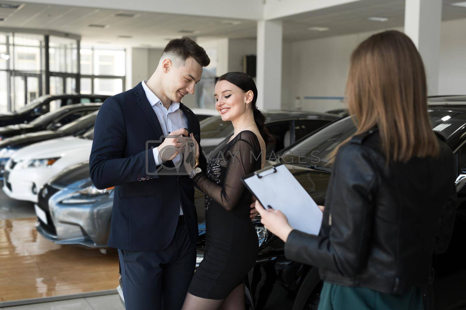 Royalty free image of A couple of men and women are happy to buy a new car in a car dealership with the seller by StudioPeace