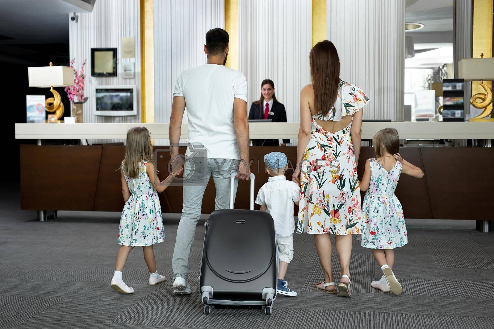 Royalty free image of Family of five enters to the hotel lobby to check in at the reception for vacation by StudioPeace