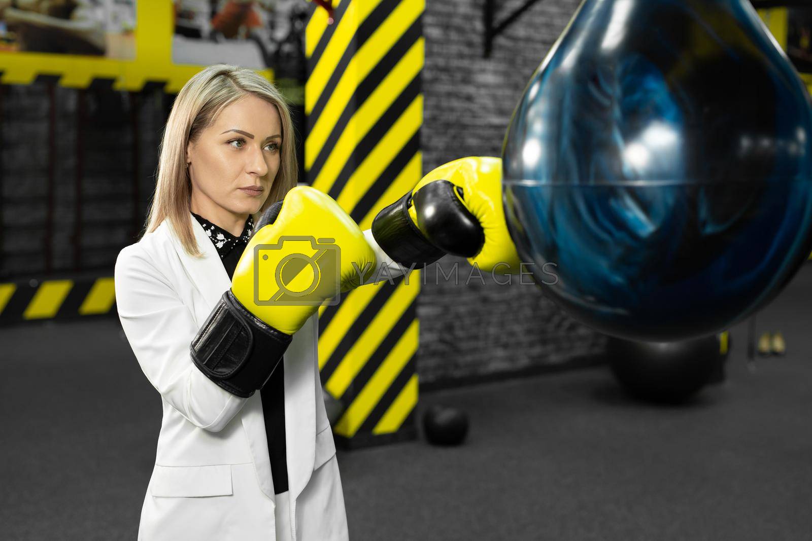 Royalty free image of Young female businesswoman in a white suit hits a punching bag in the gym. The concept of office employee anger and relaxation by StudioPeace
