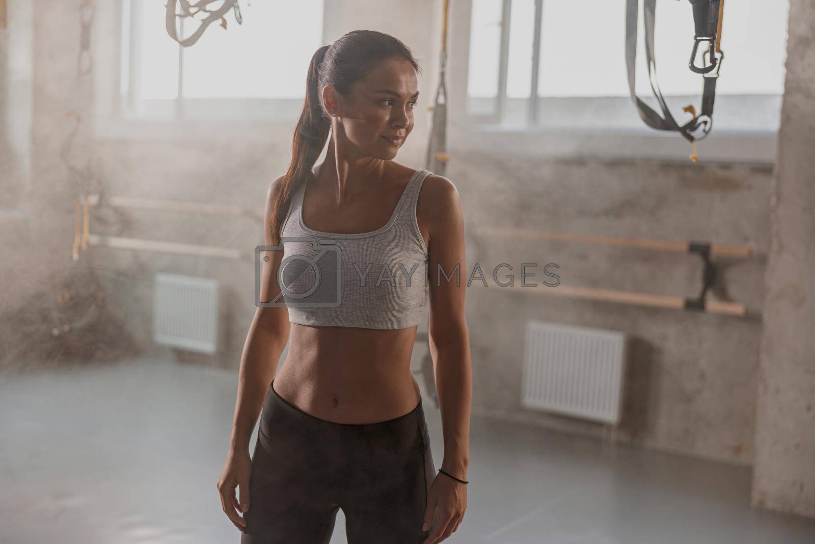 Caucasian fitness woman in black leggings and topic looking to side while posing in gym club