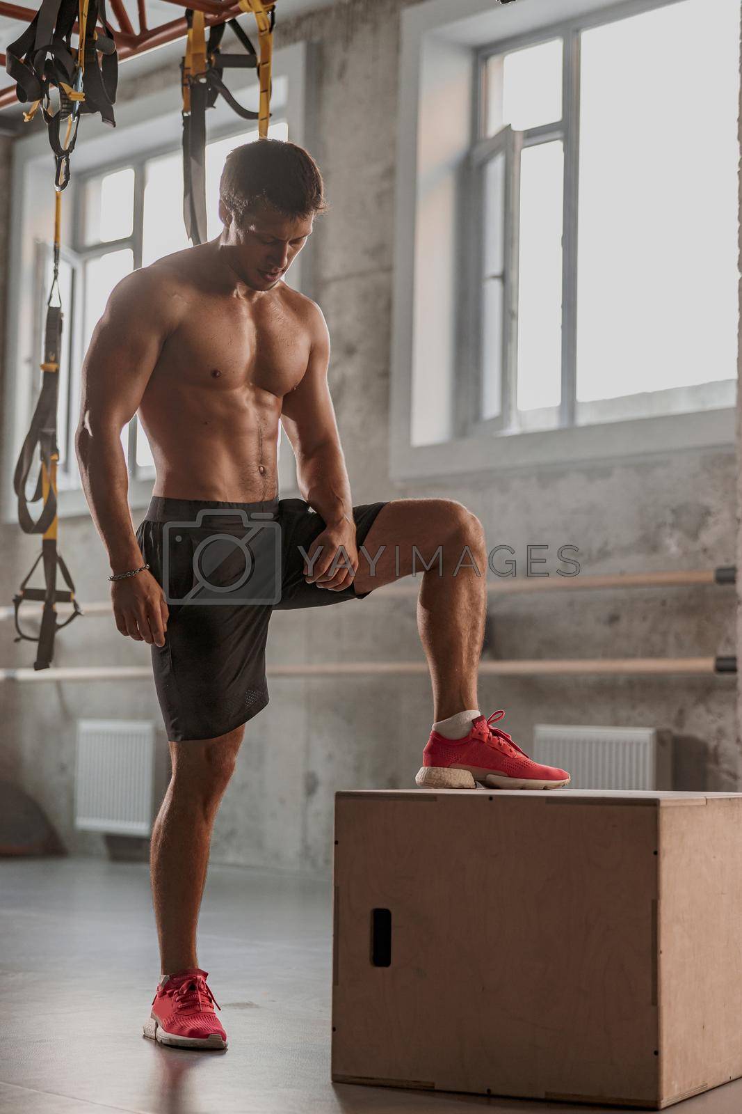 Sporty physically fit man doing step-up exercise on feet box while doing gym training in sports club