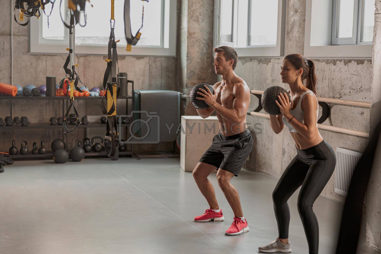 Concentrated sporty man and woman with athletic bodies working out with exercise ball in gym club