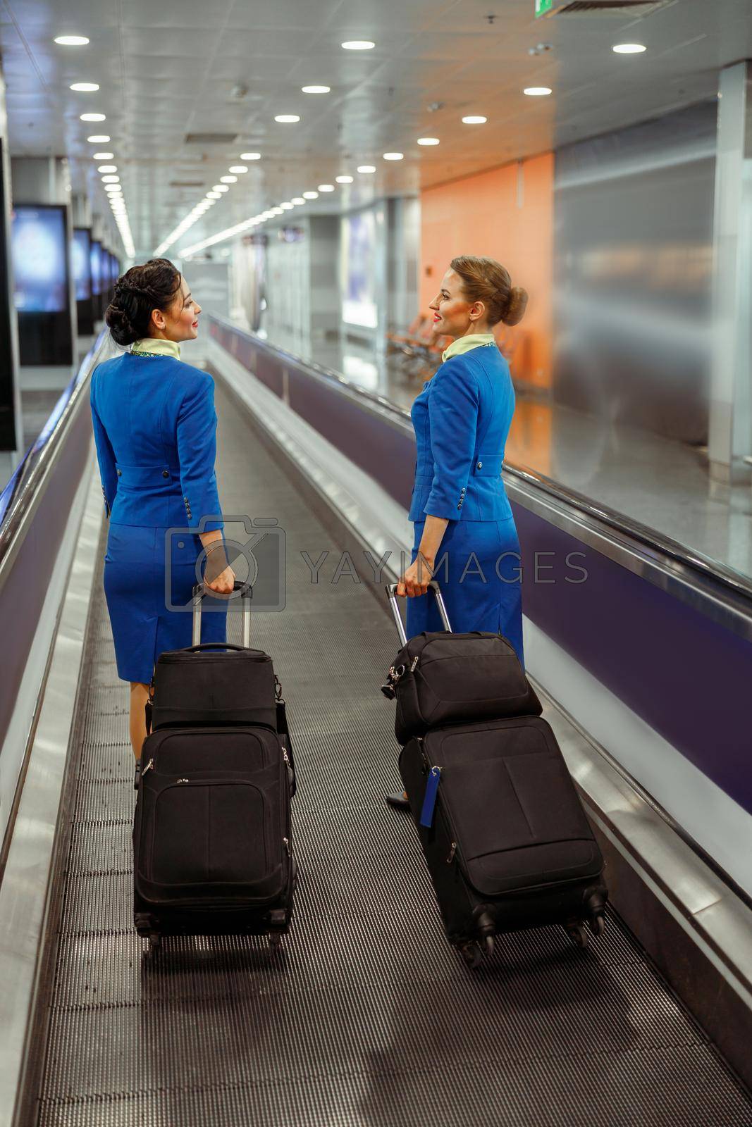 Women stewardesses with trolley luggage bags walking down airport terminal