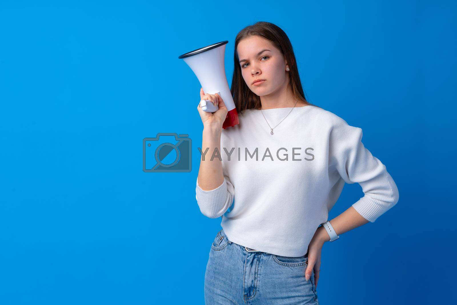 Royalty free image of Teen girl making announcement with megaphone at blue studio by Fabrikasimf