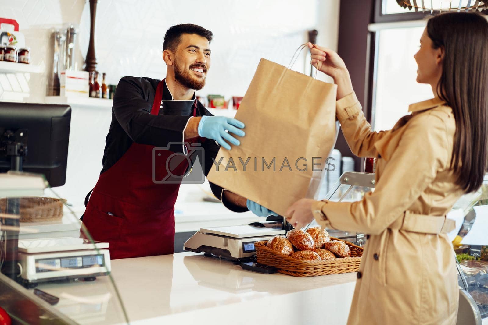 Royalty free image of Shop assistant handling shopping bag to female customer in grocery store by Fabrikasimf