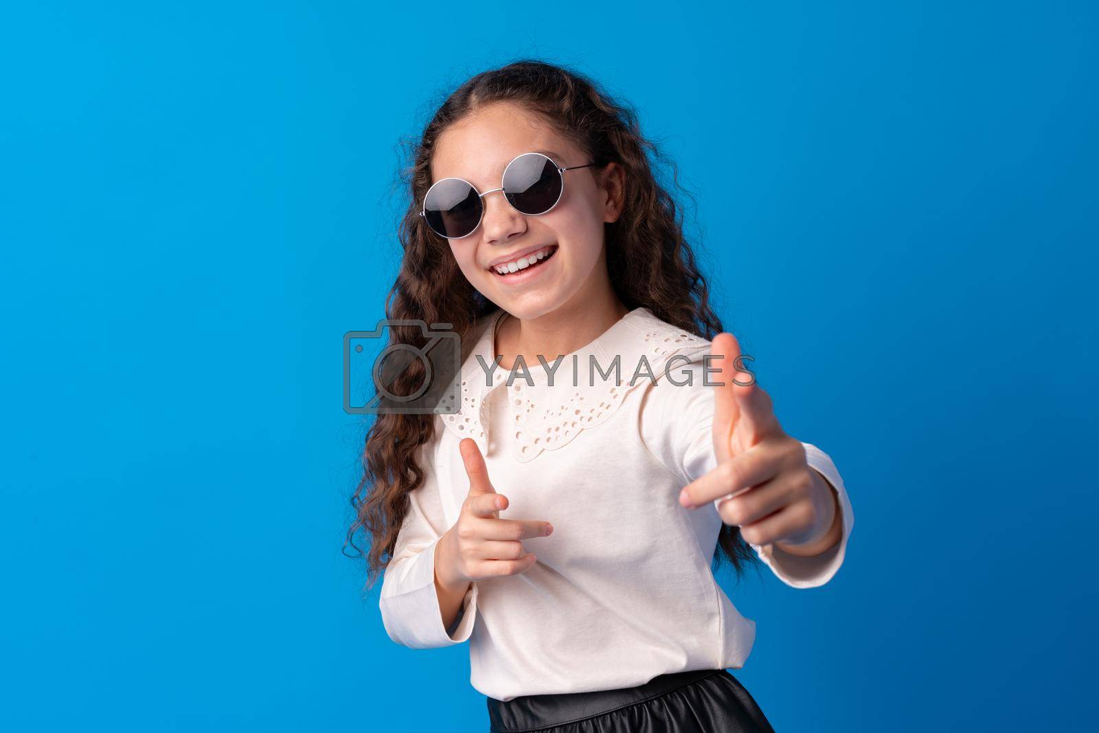 Little fashion girl in sunglasses against blue background, close up
