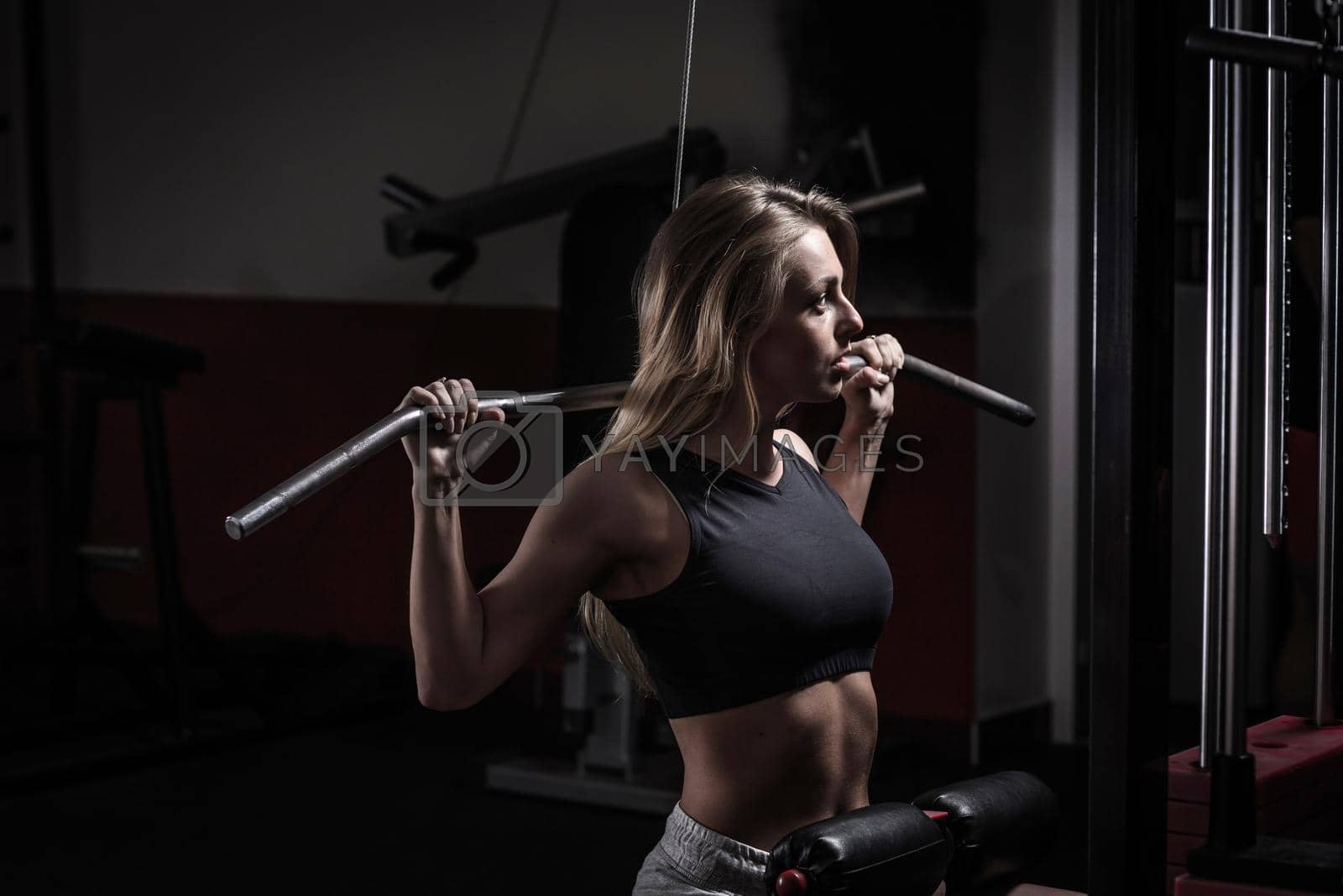 Young business woman doing exercise on a fitness machine in a fitness club. Photo on a dark background.