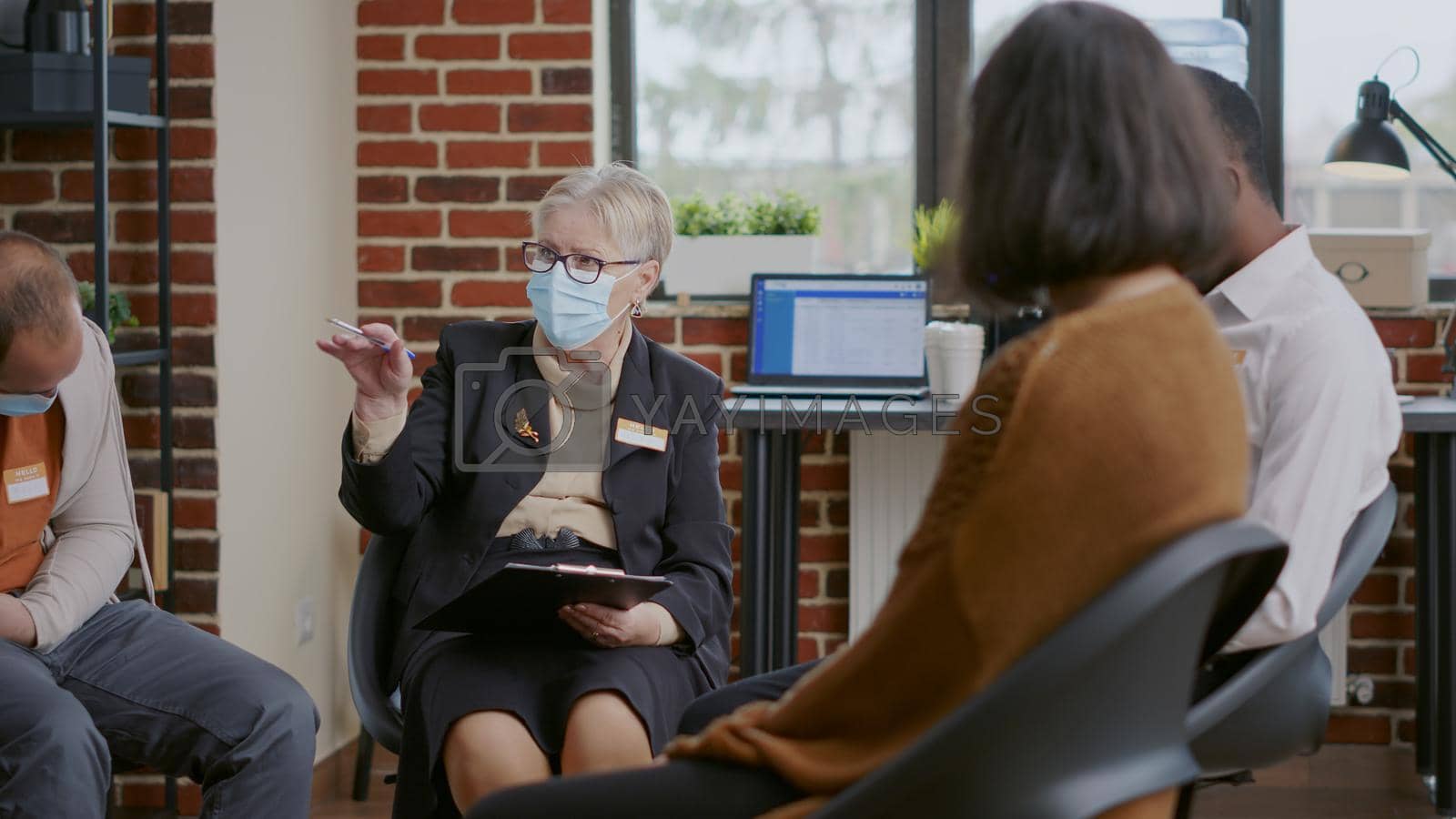 Royalty free image of Close up of woman psychiatrist talking to people at aa group therapy, wearing face mask by DCStudio