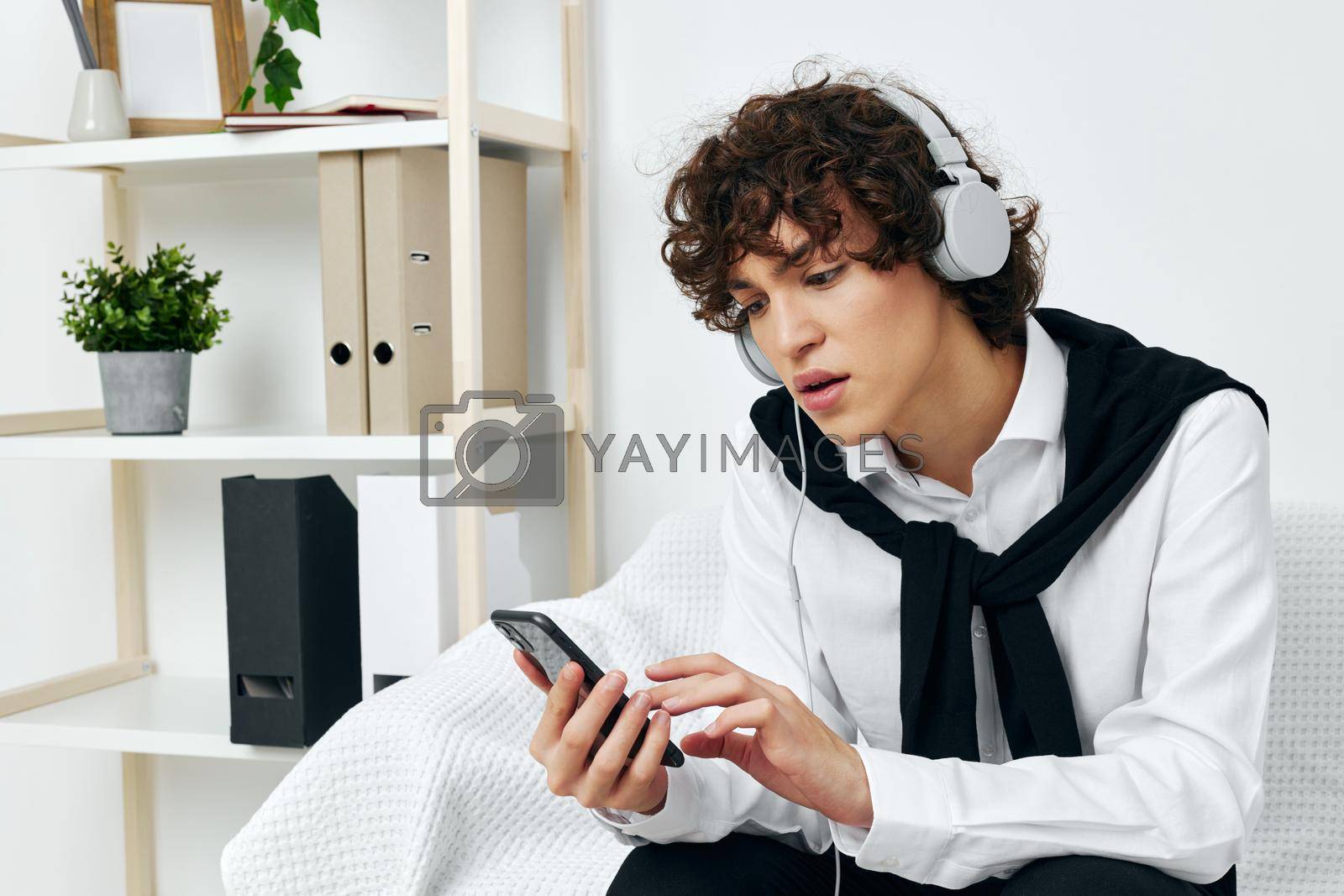 teenager in headphones sitting on a white sofa smartphone communication. High quality photo