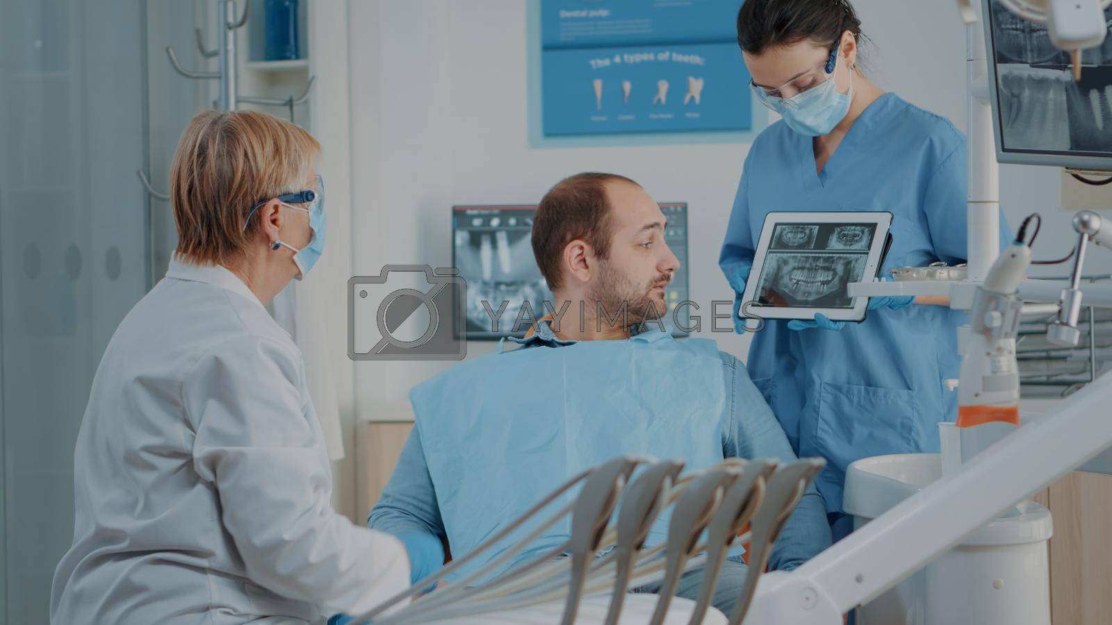 Dentist and nurse showing x ray results to patient with toothache, explaining dental procedure and diagnosis. Stomatology team analyzing radiography to do oral care surgery on man.