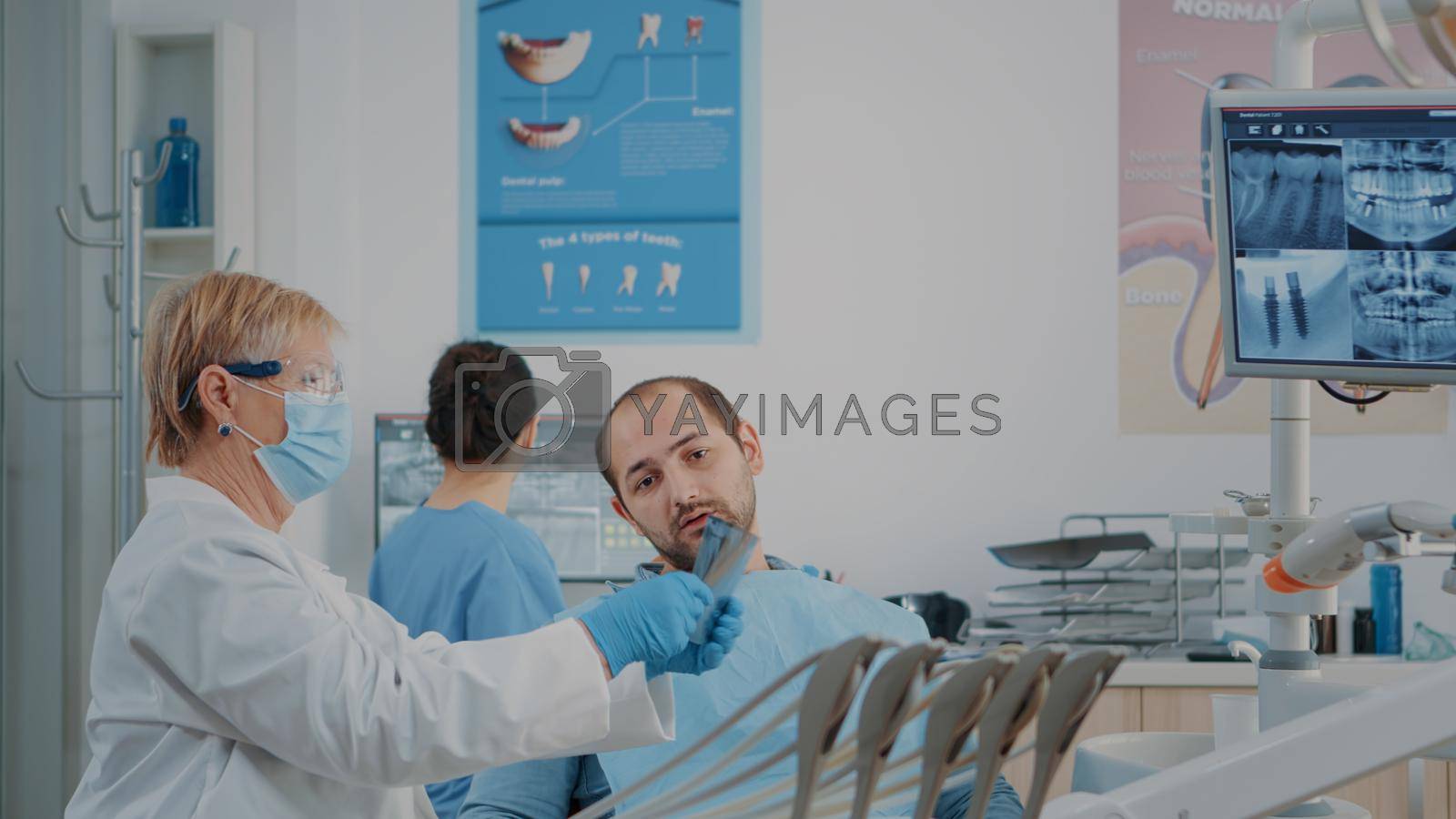 Senior dentist explaining teeth radiography to patient with caries problems. Stomatologist using x ray scan results to do dental examination and drill procedure at dentistry checkup.