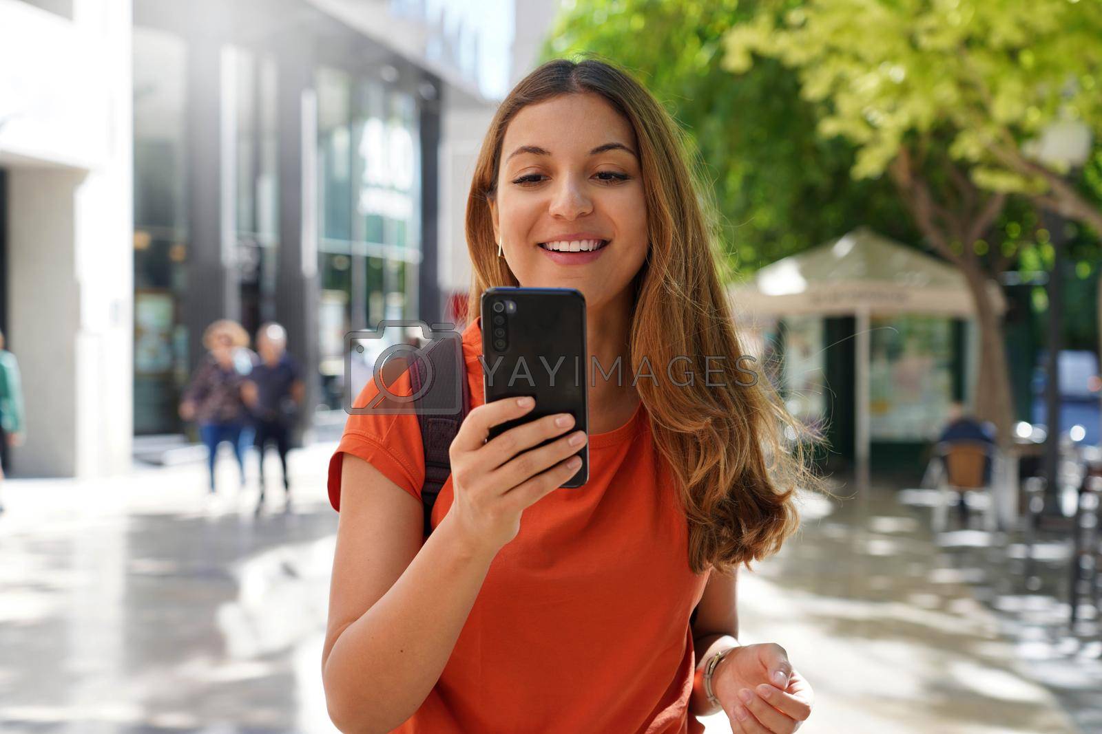 Portrait of happy young fashion woman watching at mobile phone in city