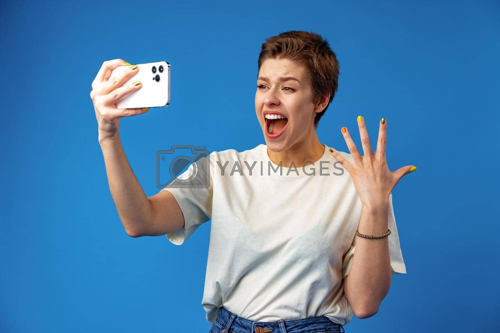 Royalty free image of Shocked girl with short hair looking at phone screen with mouth open over blue background by Fabrikasimf