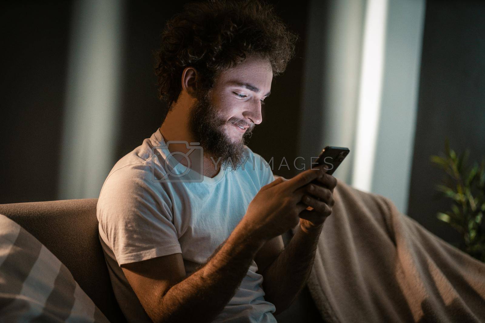 Royalty free image of Nice Guy Texting to his Girlfriend by his Smartphone in the evening. Before Going to Bed he Sends a Mail to his Sister. Close-up. by LipikStockMedia