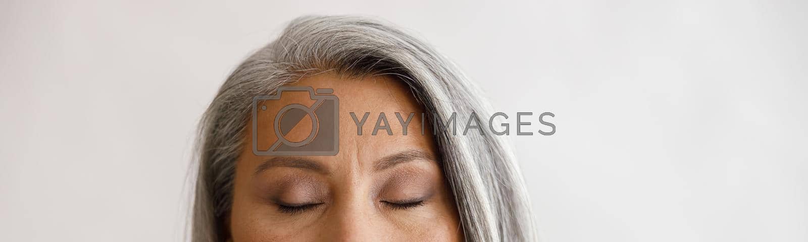 Royalty free image of Tranquil grey haired lady with closed eyes and elegant makeup poses on light background by Yaroslav_astakhov