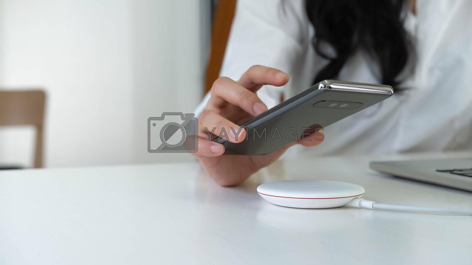 Royalty free image of Working Woman putting smartphone on wireless charger in office by nateemee