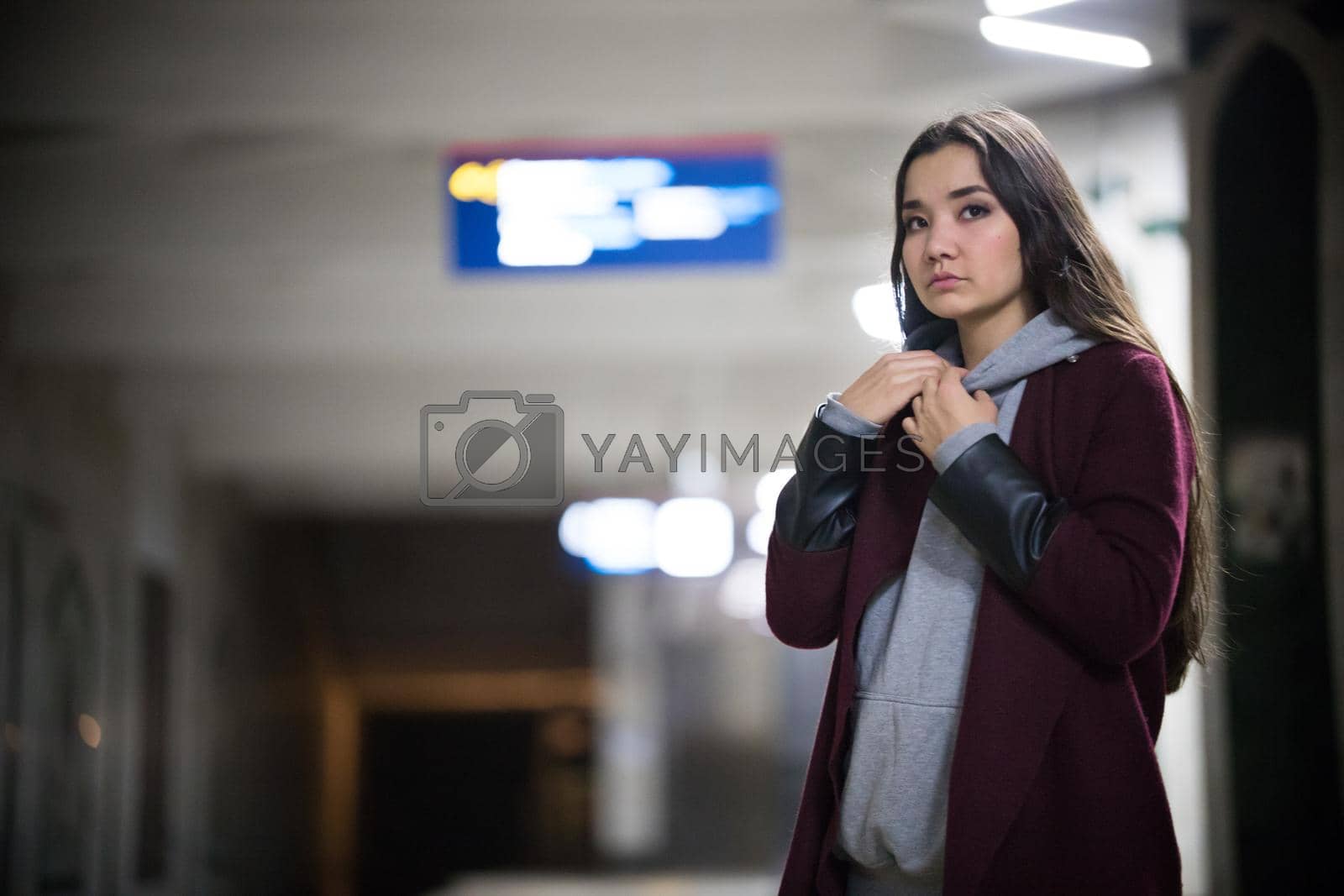 Young pretty woman waiting for the train in subway platform. Night. Looking to the side