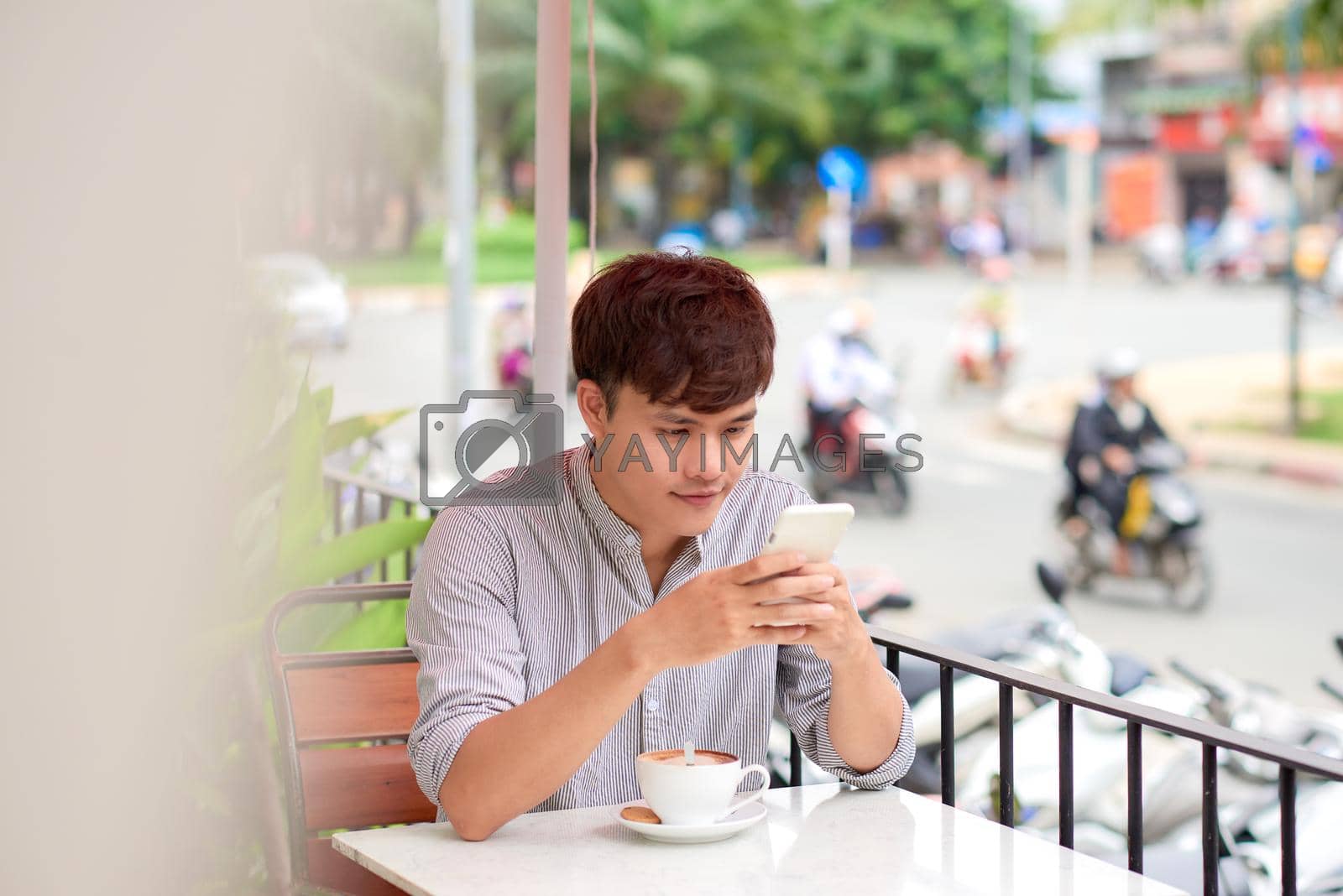 Royalty free image of Young smiling man looking on the phone or reading message in cafe outdoor by makidotvn