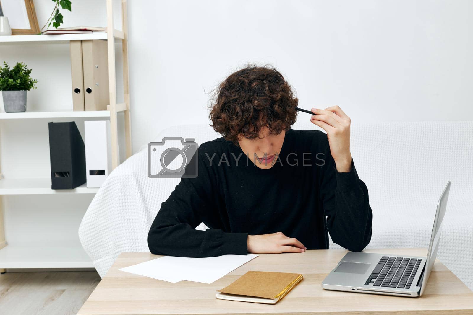 curly guy sitting at the table in a black sweater lessons communication. High quality photo