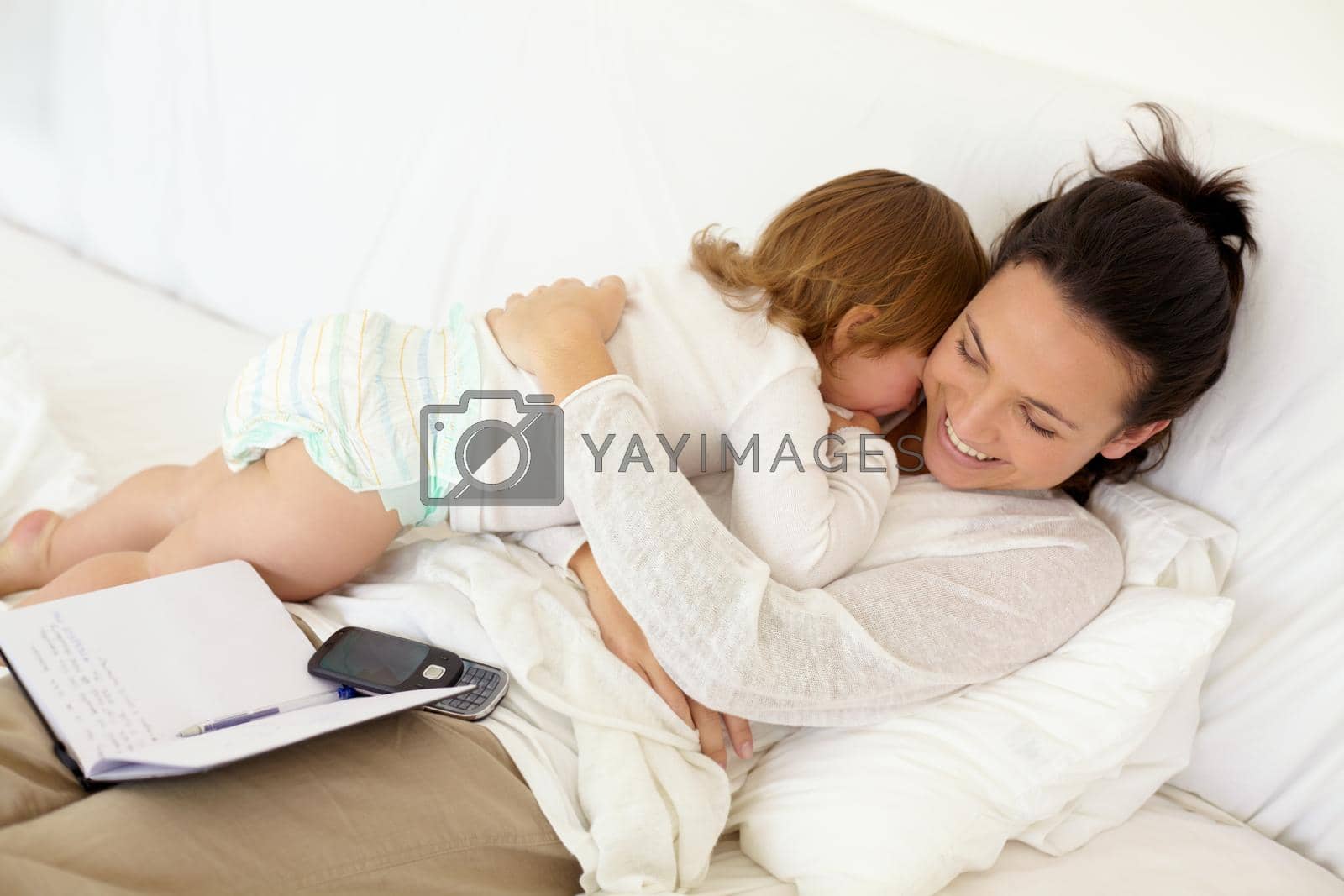 Royalty free image of I always have time for you. A young mother lying in bed and giving her toddler a hug with an open notebook lying on her back. by YuriArcurs