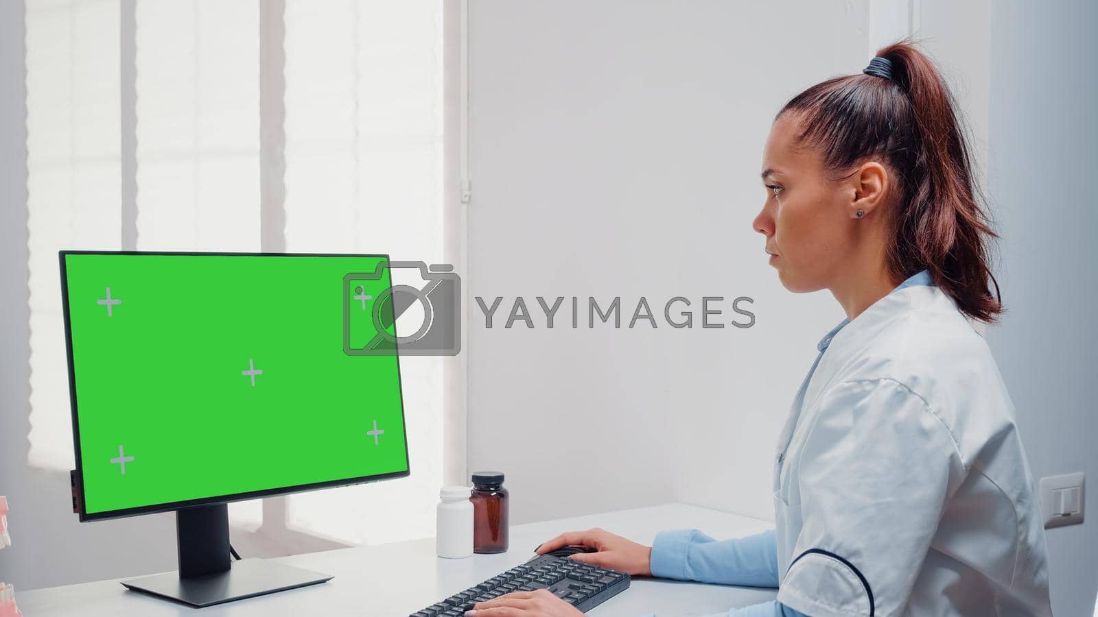Dentist working with horizontal green screen on computer for teethcare at dental office. Woman using keyboard and monitor with chroma key for mockup template and isolated background