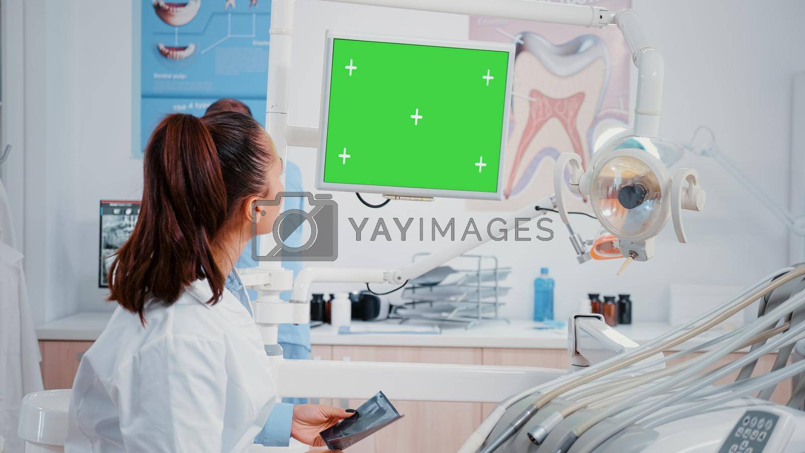 Dentist looking at monitor with horizontal green screen for oral care at dental office. Woman working as stomatologist with mockup template and isolated background for teethcare