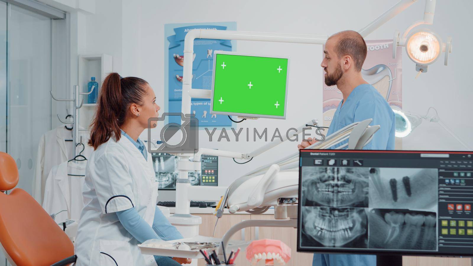 Dentist and assistant looking at green screen on monitor in dental cabinet. Teethcare specialists using chroma key and isolated mockup template for oral care, having dentistry tools
