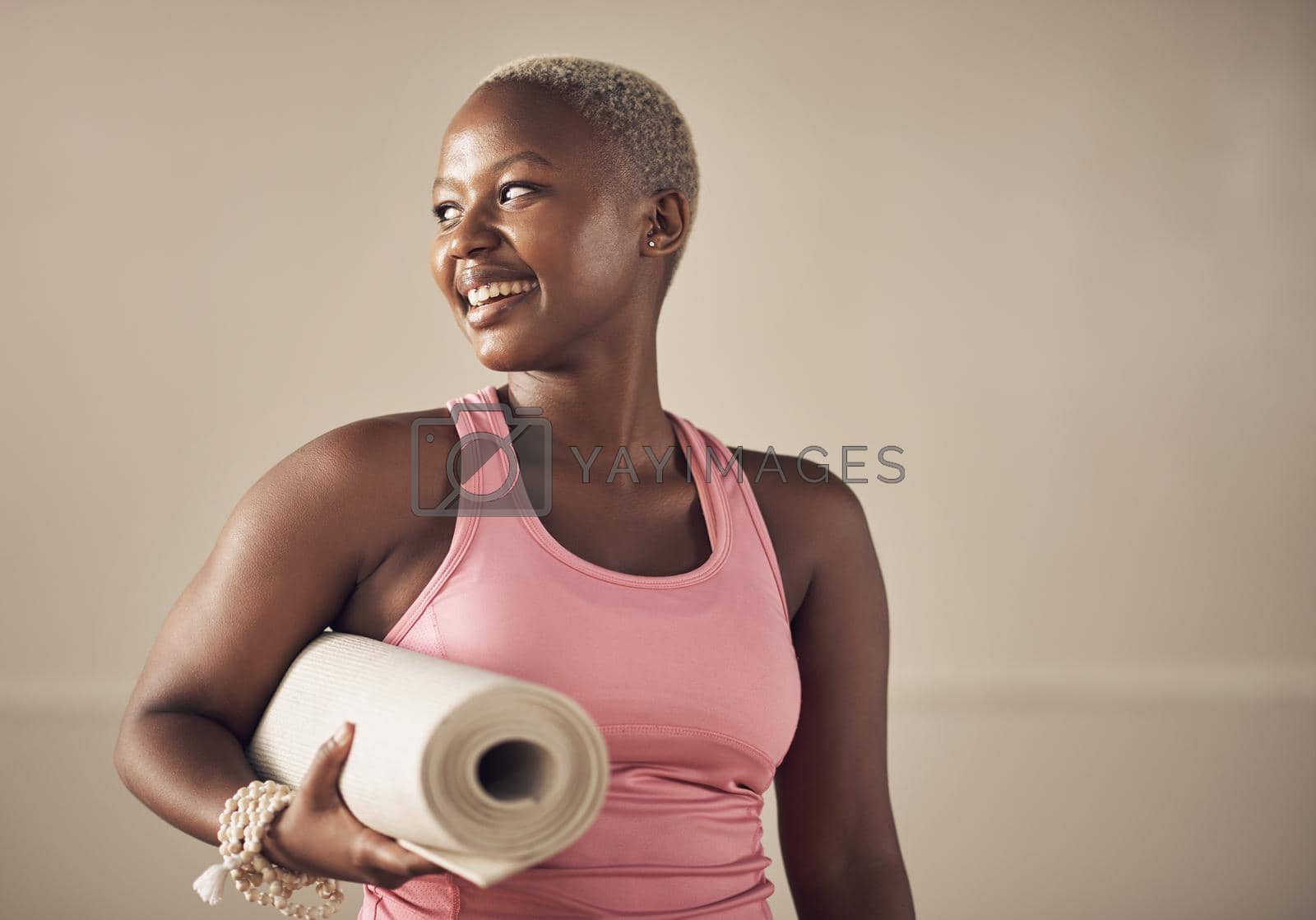 Cropped shot of an attractive young woman standing alone and holding her yoga mat before an indoor yoga session.