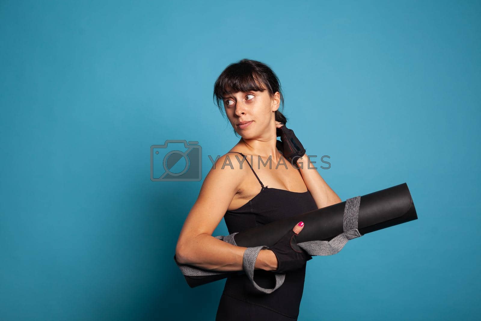 Athletic person holding yoga mat after finising fitness workout practicing strench exercices. Personal trainer stretching arm muscles working at body endurance practicing sport activity