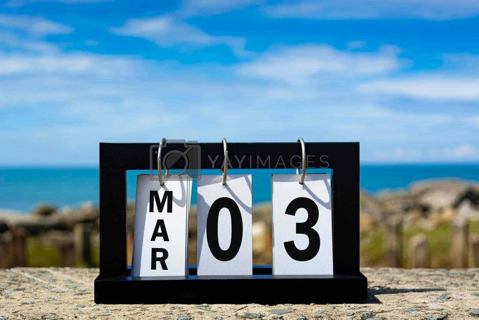 Royalty free image of Mar 03 calendar date text on wooden frame with blurred background of ocean by JennMiranda